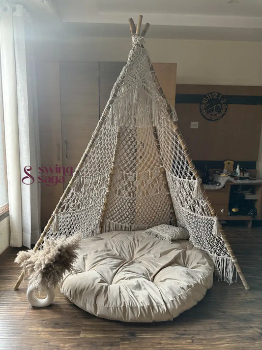 Macrame handmade teepee in white color with white mattress placed on a wooden floor.