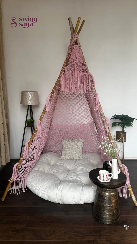 handmade macrame teepee in pink color with cushion and mattress placed in a room setting with wooden flooring.