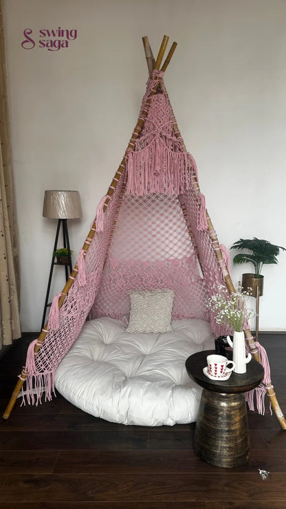 handmade macrame teepee in pink color with cushion and mattress placed in a room setting with wooden flooring.