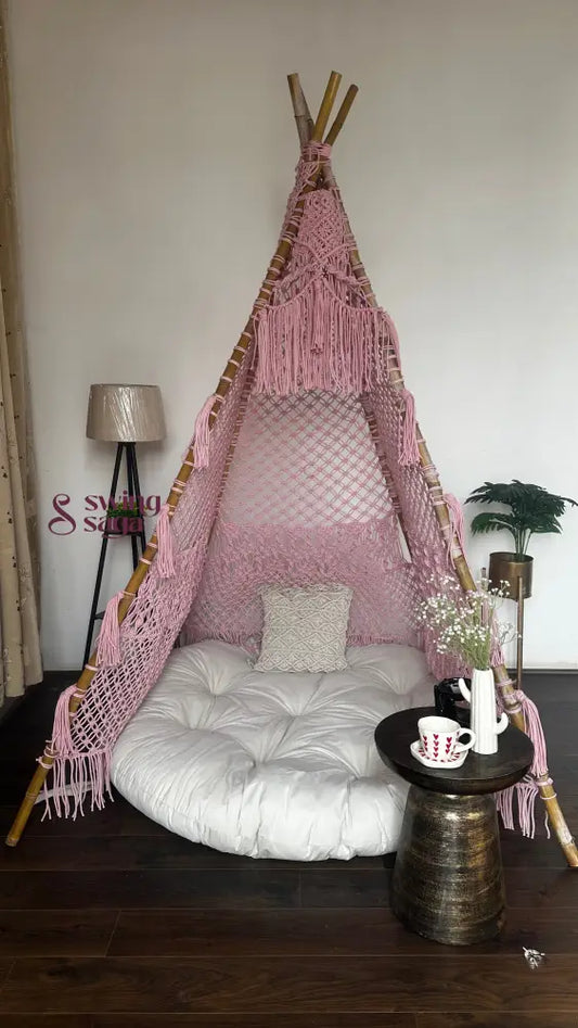 handmade macrame teepee in pink color with cushion and mattress placed in a room setting with wooden flooring.