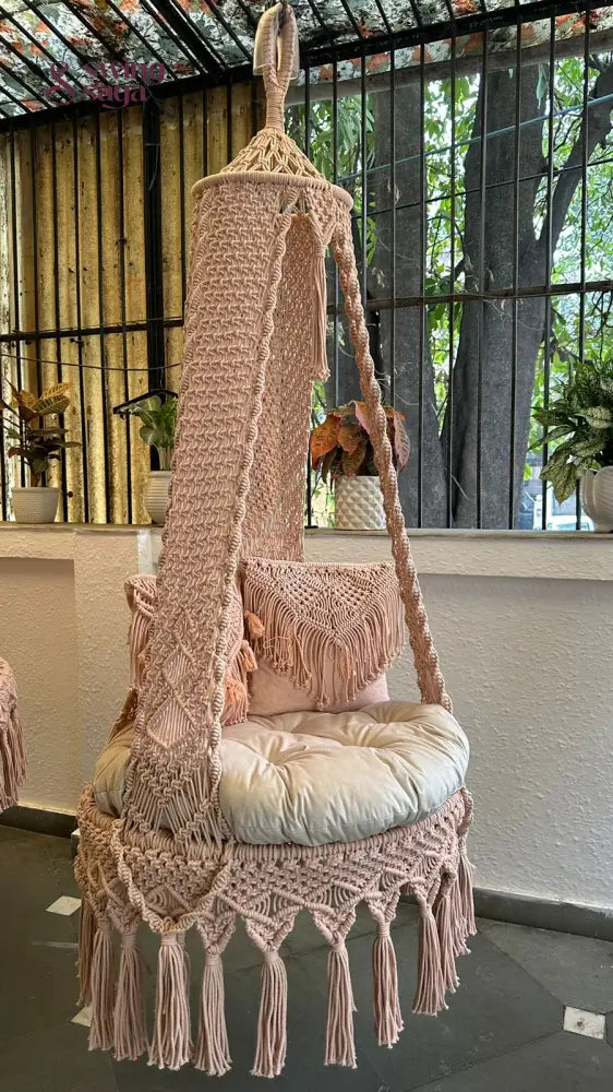 Single seater macrame hanging swing with two square shaped cushions.