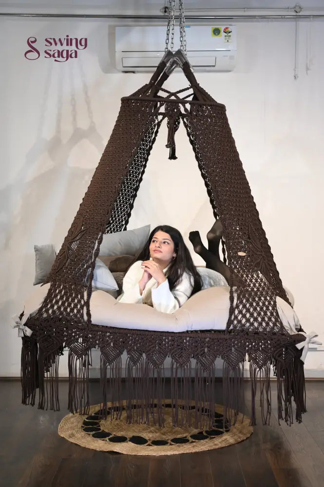 Macrame hanging square bed swing with jute rug in indoor setting. 