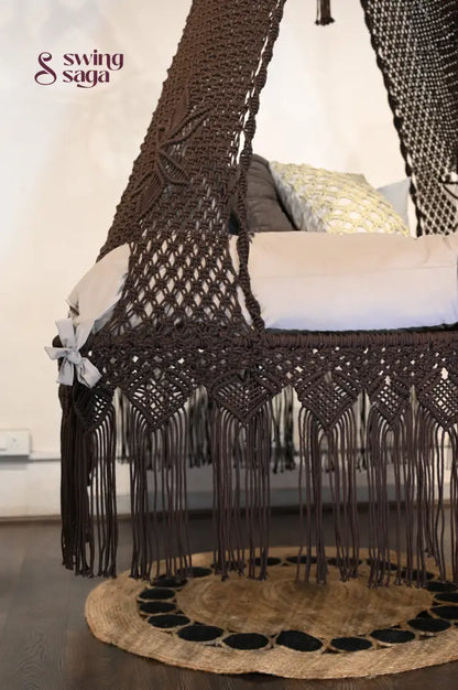 Macrame swing in coke color   with fringes at the bottom places on the jute rug.      