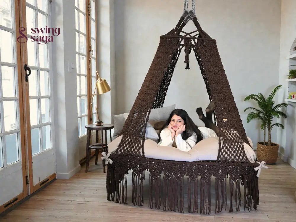 A girl resting on a square shaped b ed swing in cocoa color in indoor setting.