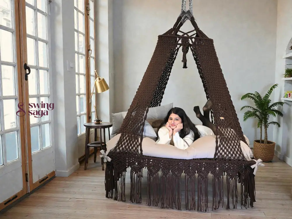 A girl resting on a square shaped b ed swing in cocoa color in indoor setting.