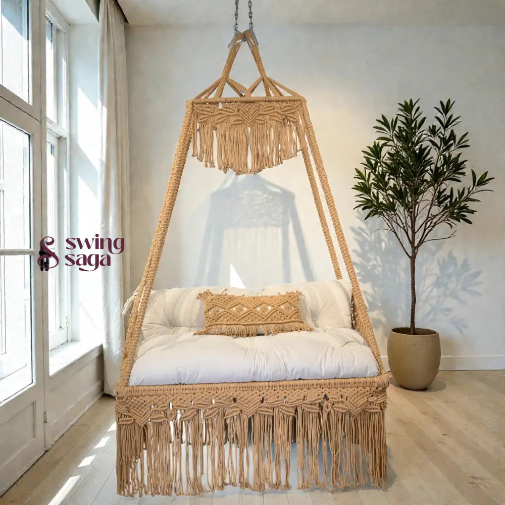 Macrame sofa swing with white cushion and decorative pillows in a bright room with a plant.