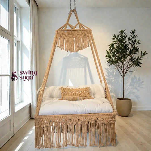 Macrame sofa swing with white cushion and decorative pillows in a bright room with a plant.