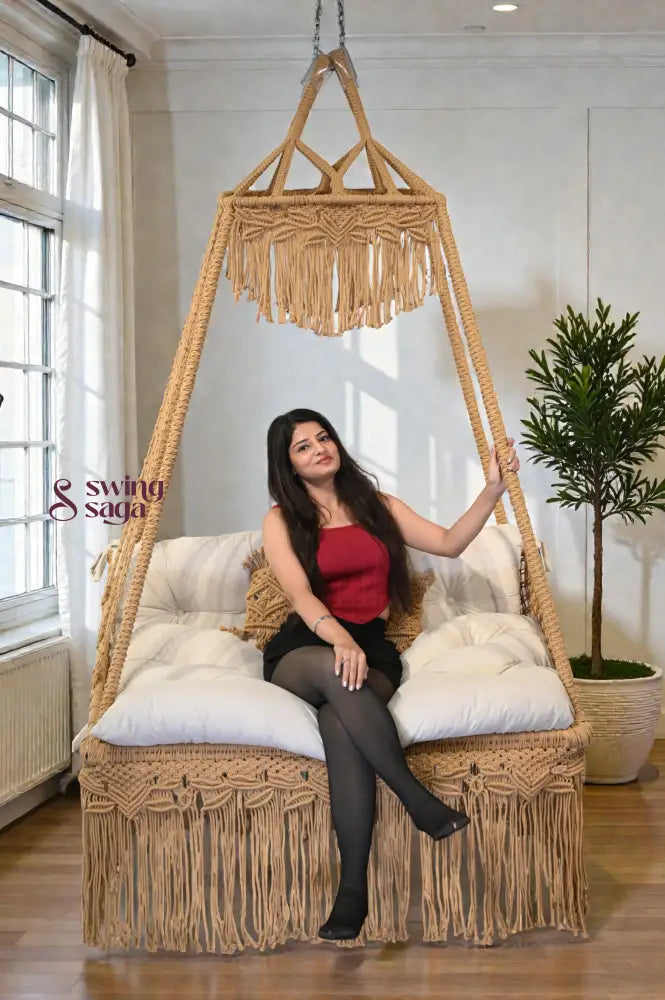 Woman sitting in a macrame swing in a bright room with large windows.