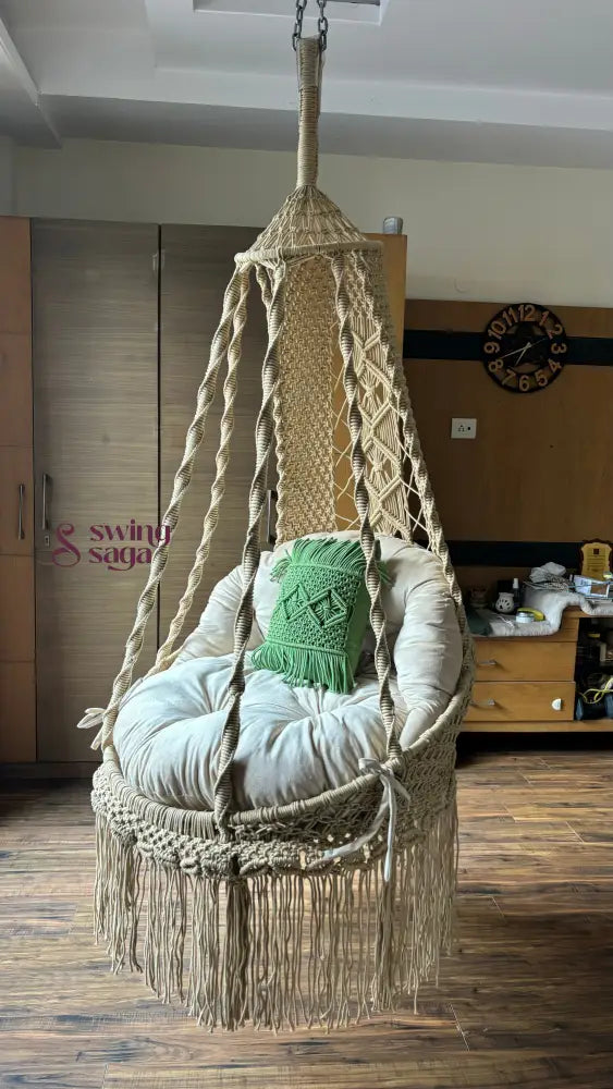 Hanging macrame chair with cushions in a cozy room setting.