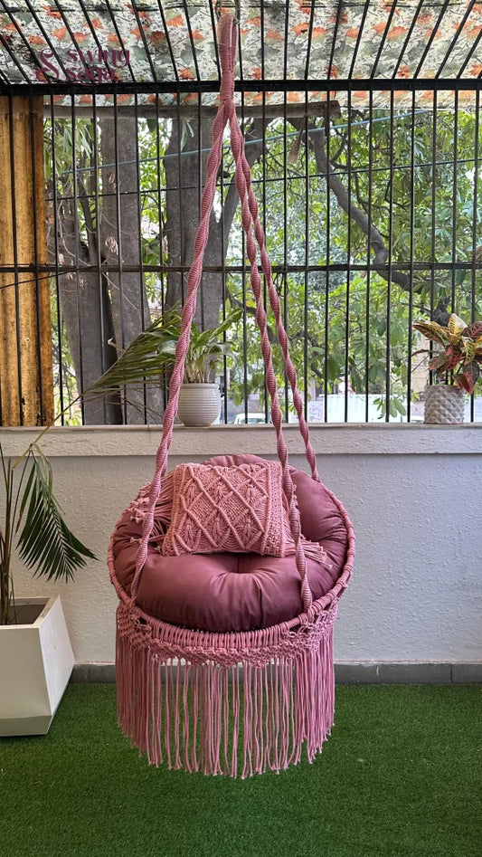 macrame chair swing in pink color hanging in a garden area.