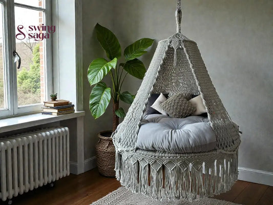 Grey colored macrame hanging swing with cushions on a mattress. 