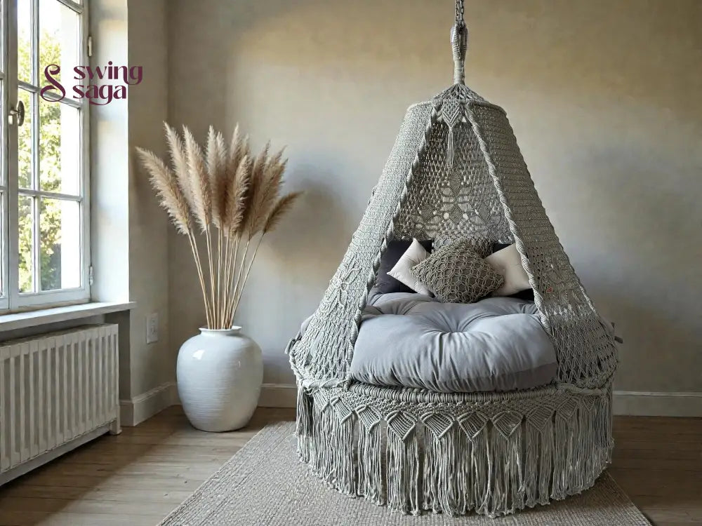 Grey colored macrame swing with mattress for sitting in an indoor room corner with rug. 