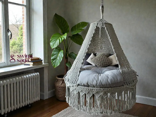 Grey colored macrame hanging swing with cushions on a mattress. 