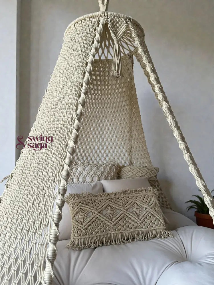 Macrame bed swing with pillows and a plant in the corner.