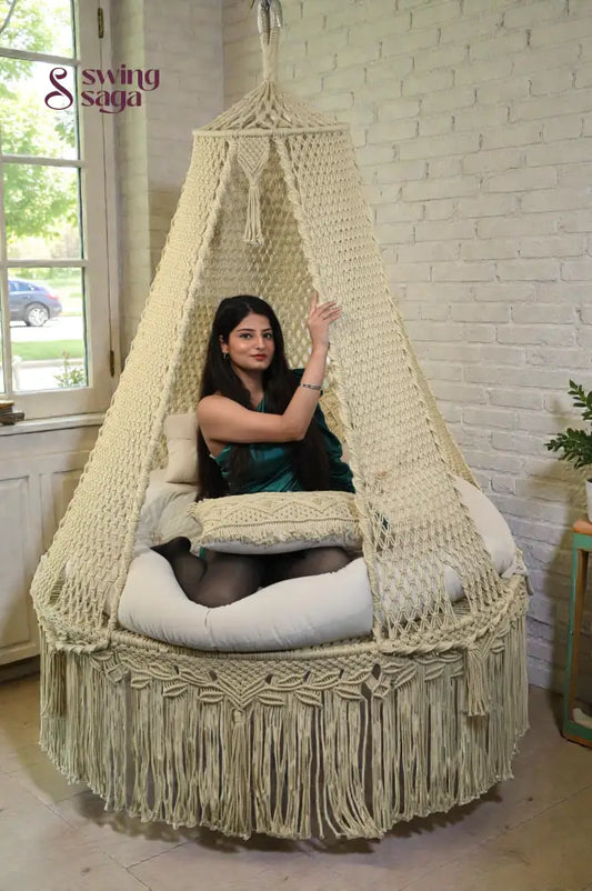 Woman sitting in a macrame hanging swing with a white brick wall background