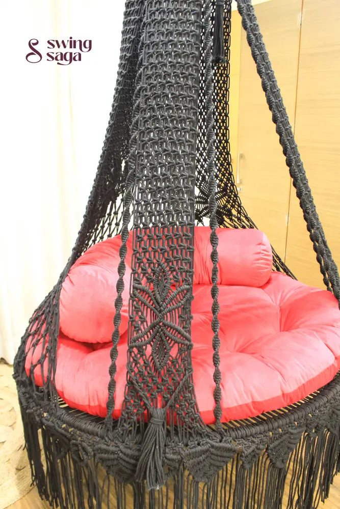 Macrame hanging swing with red mattress and cylindrical cushion.