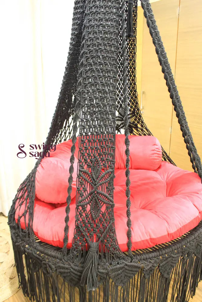 Macrame hanging swing with red mattress and cylindrical cushion.