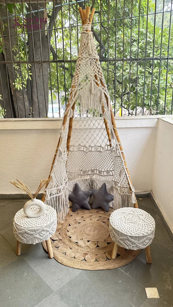 Handmade macrame teepee in white color with a pair of ottoman placed in an outdoor setting.