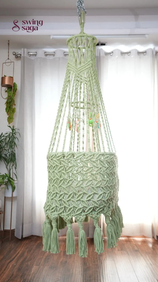 Side image of a lime green colored macrame baby cradle in a room setting.