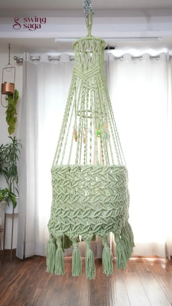 Side image of a lime green colored macrame baby cradle in a room setting.