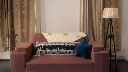 Maroon sofa with decorative pillows in a room with curtains and a lamp.