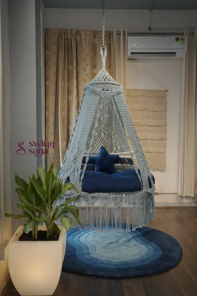 Hanging chair with a blue cushion on a wooden floor next to a plant and rug.