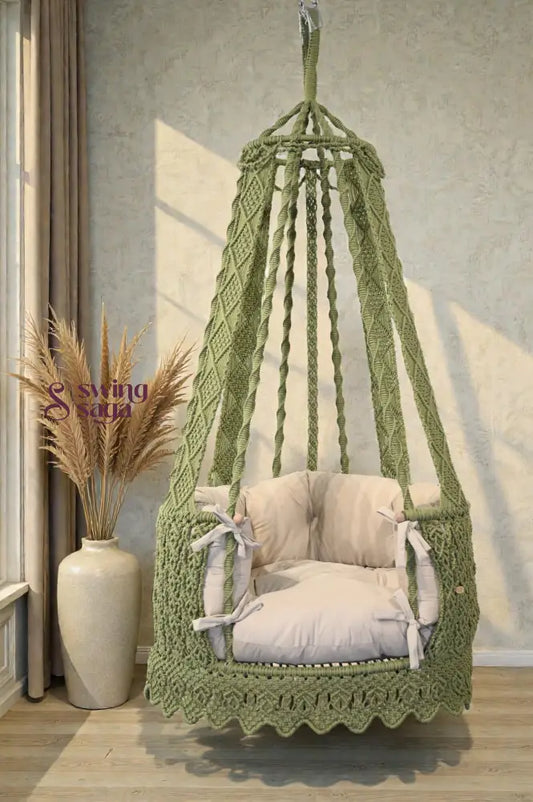 Green hanging chair swing with cream mattress with a pampas grass vase in background.