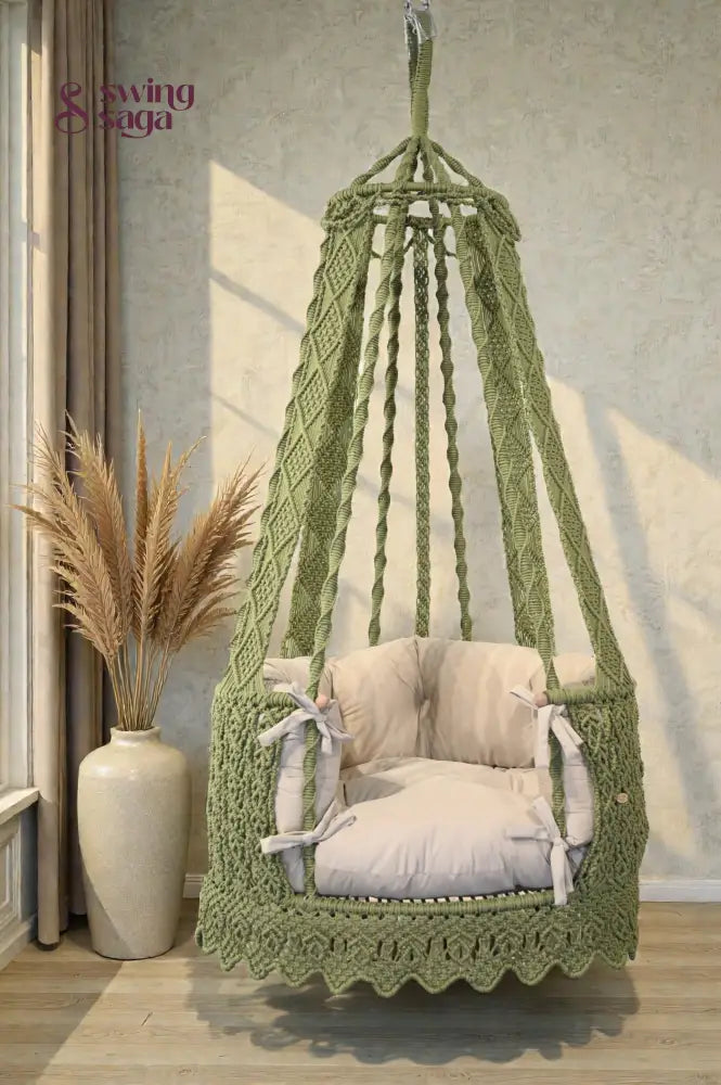 Green hanging chair swing with cream mattress with a pampas grass vase in background.