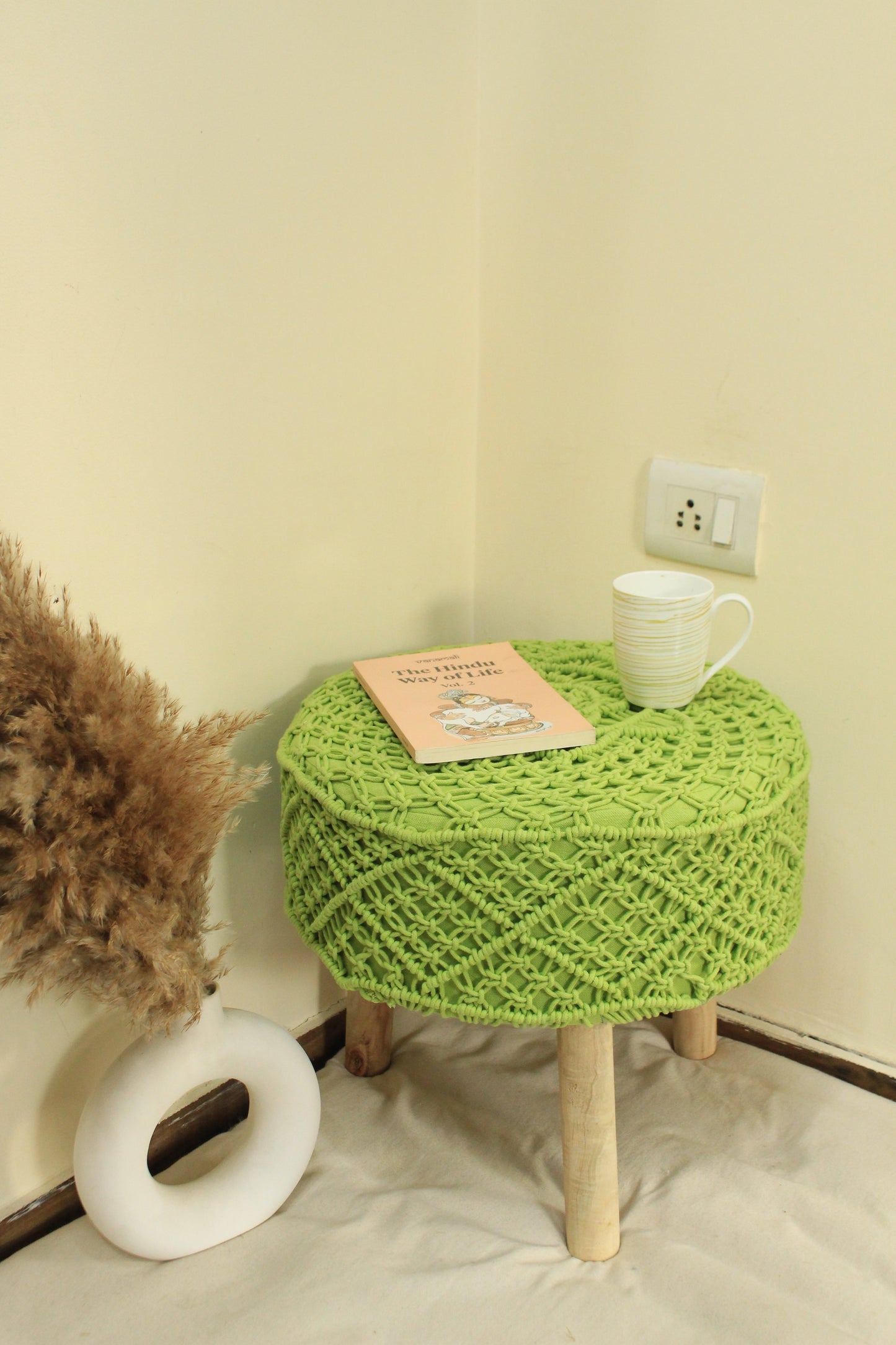 green ottoman macrame with three wooden legs.