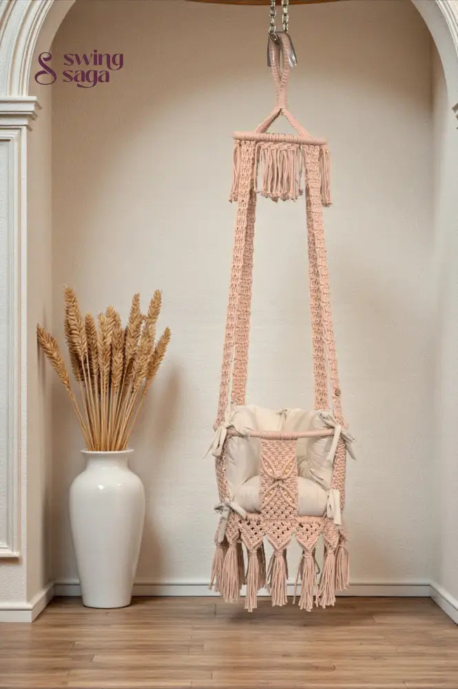 Macrame Baby Swing with tassels hanging in a room with a vase of dried plants.