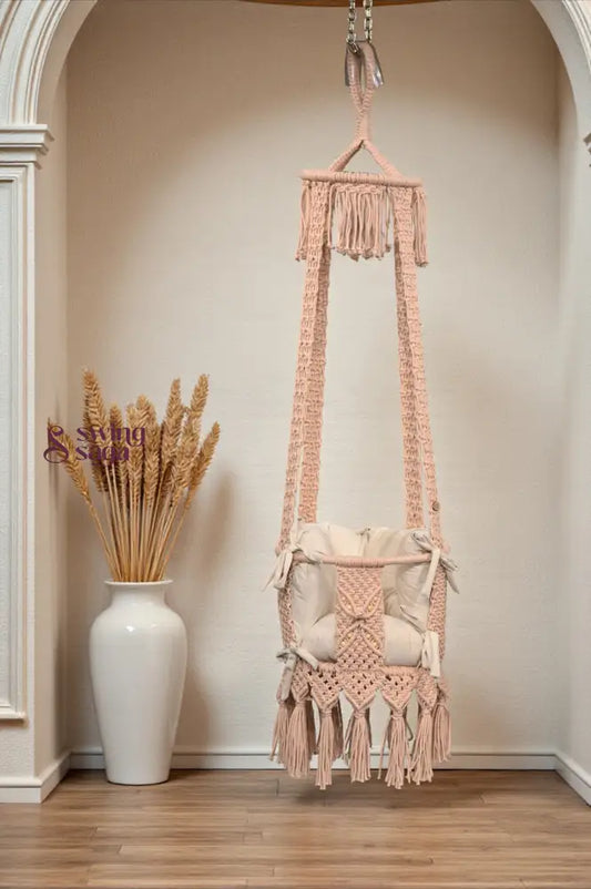Macrame Baby Swing with tassels hanging in a room with a vase of dried plants.