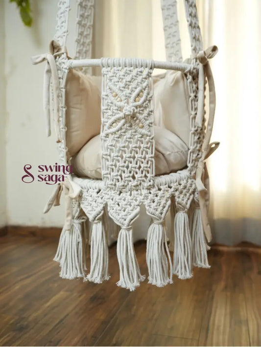 Detailed image of white colored hanging macrame baby swing with tassels. 
