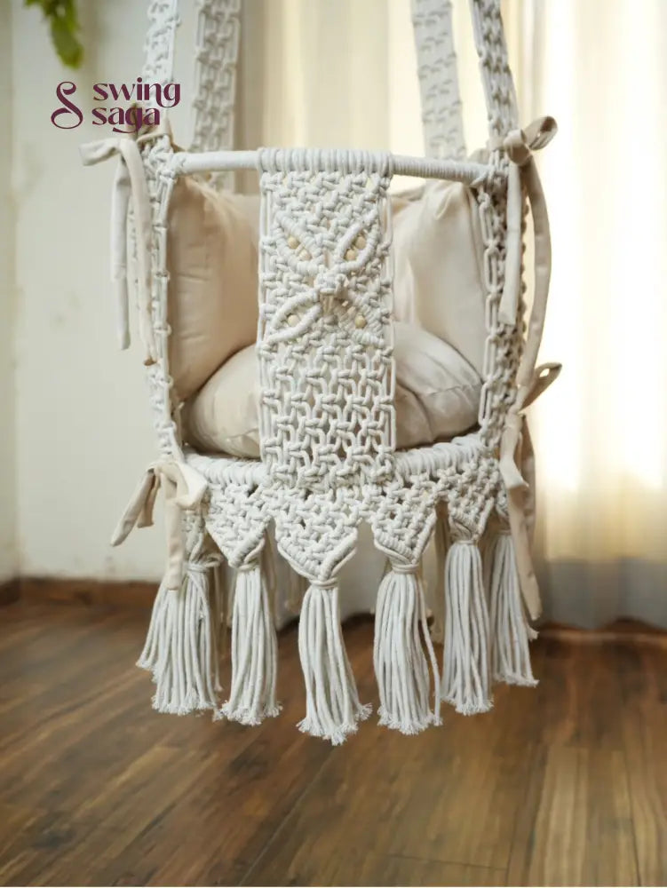 Detailed image of white colored hanging macrame baby swing with tassels. 