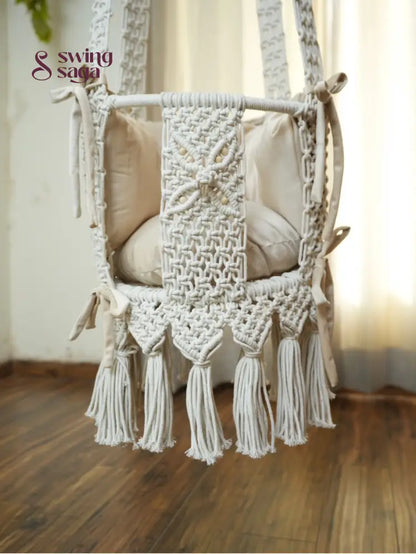 Detailed image of white colored hanging macrame baby swing with tassels. 