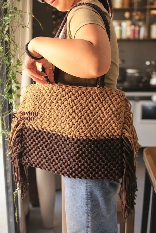 A girl holding macrame bag in brown and dark brown color. it has fringes from every side.
