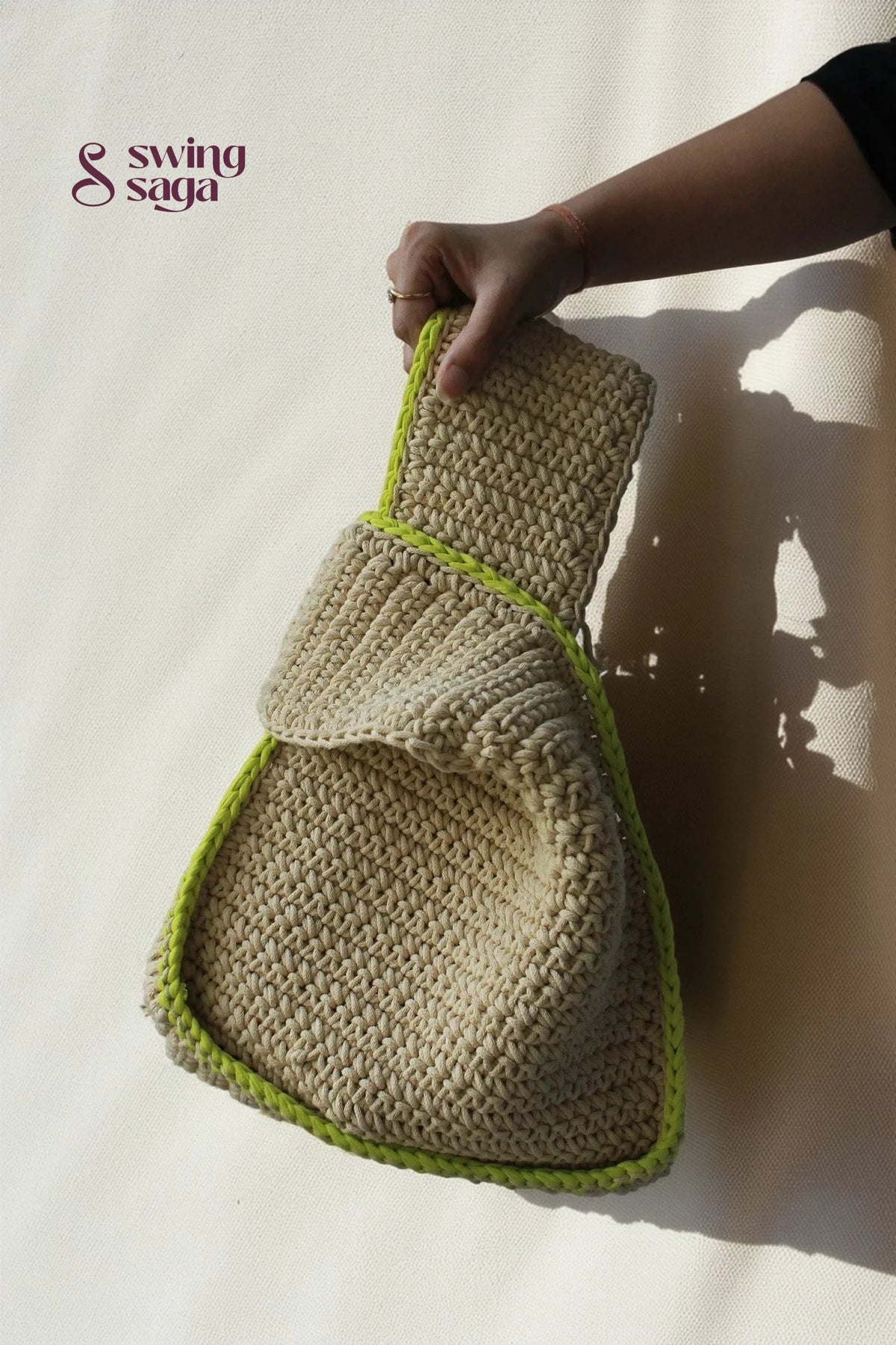 a girl holding a modern sling bag in beige color with green border.