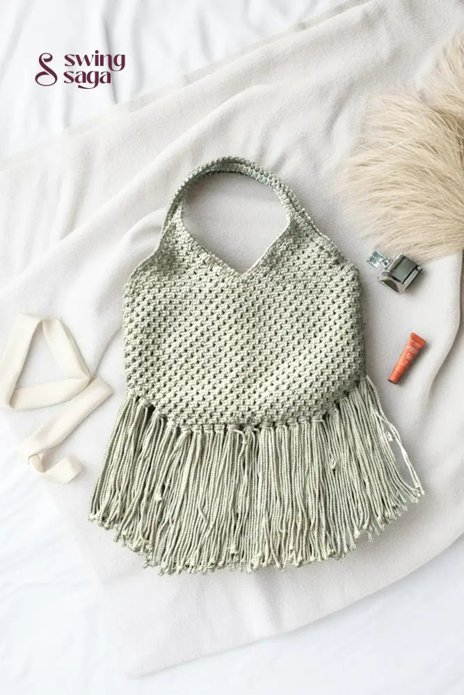 Photo of macrame bag in off white color with long fringes placed at a white background.