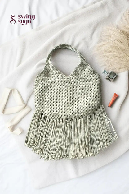 Photo of macrame bag in off white color with long fringes placed at a white background.