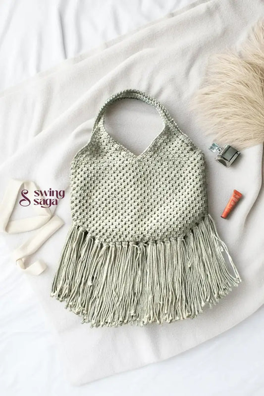 Photo of macrame bag in off white color with long fringes placed at a white background.