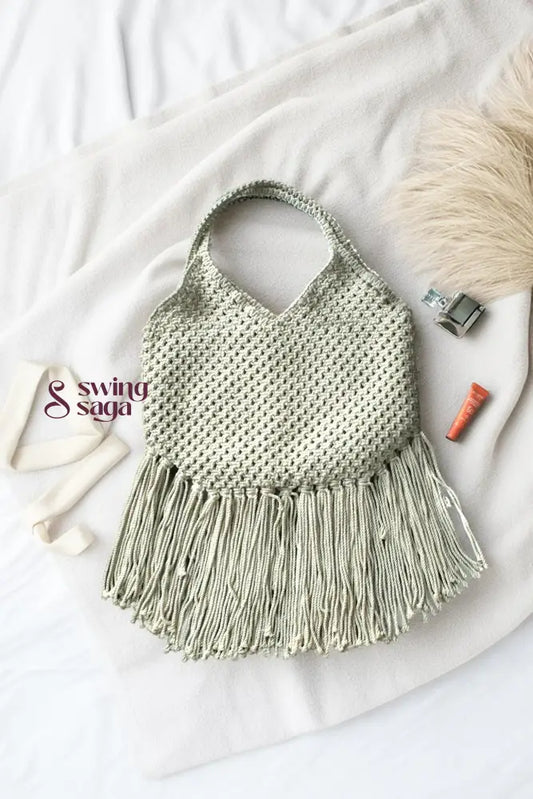 Photo of macrame bag in off white color with long fringes placed at a white background.
