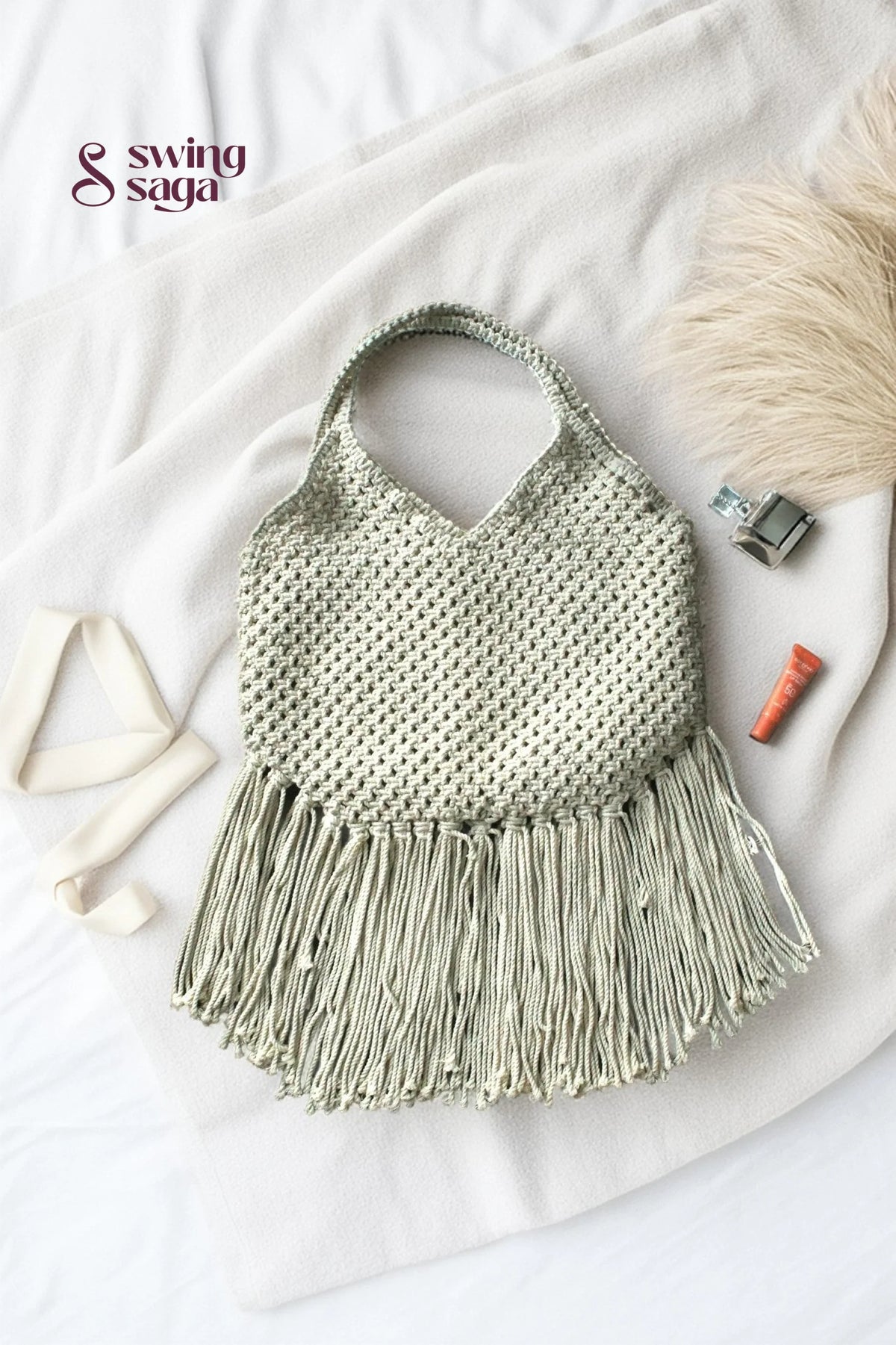 Photo of macrame bag in off white color with long fringes placed at a white background.