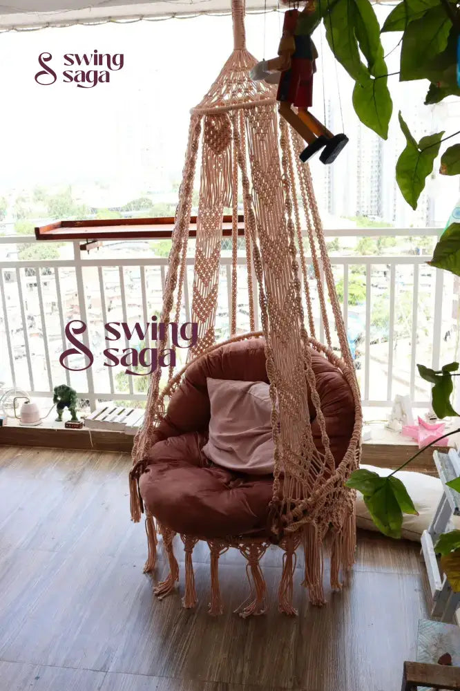 Macrame hanging chair swing with mattress and cushion in a balcony area.
