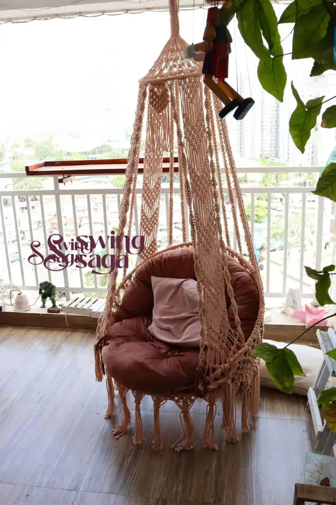 Macrame hanging chair swing with mattress and cushion in a balcony area.