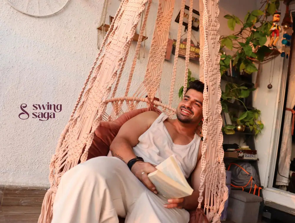 A guy on a handmade macrame swing with a book in his hand.