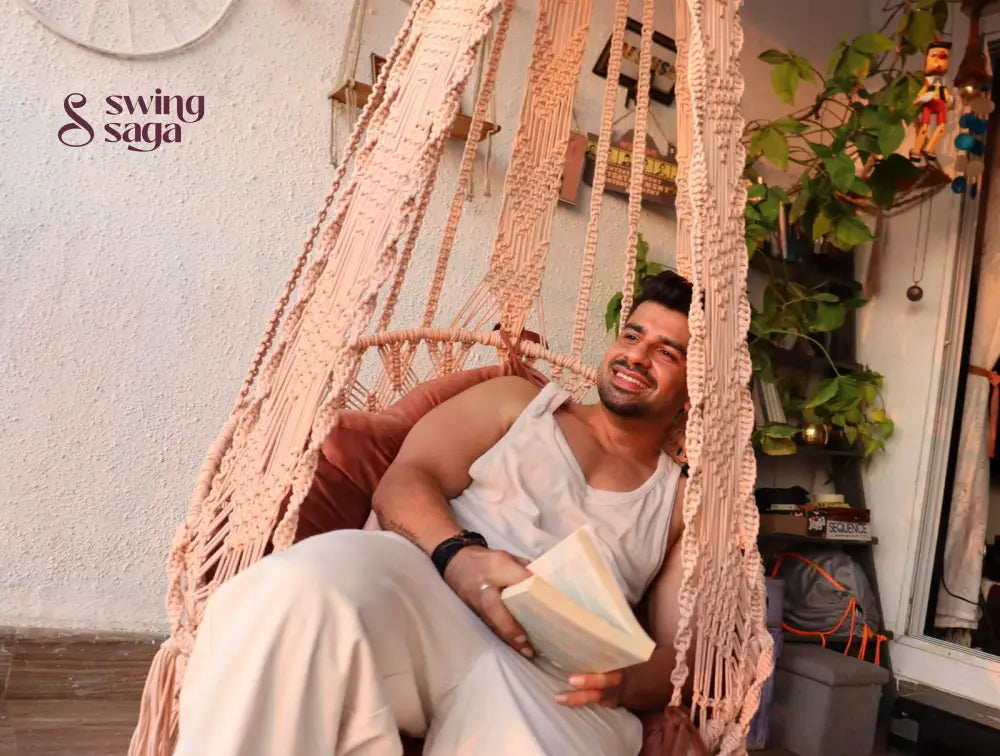 A guy on a handmade macrame swing with a book in his hand.