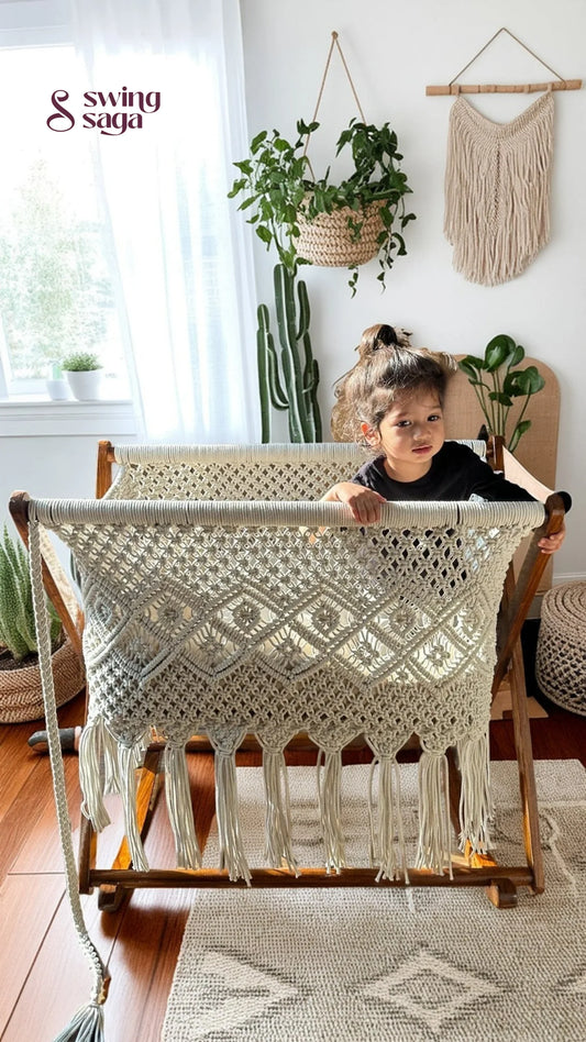 Child playing in a white macrame bassinet in a bright room with plants.