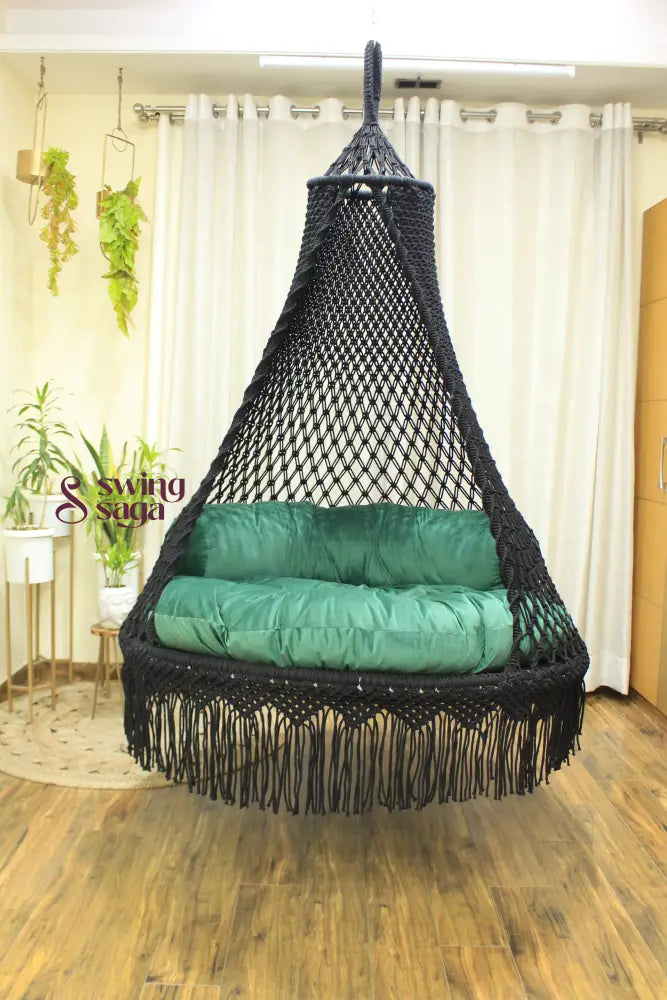 Black macrame swing with a mattress and a cylindrical cushion in  sea green color.
