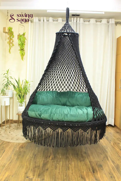 Black macrame swing with a mattress and a cylindrical cushion in  sea green color.