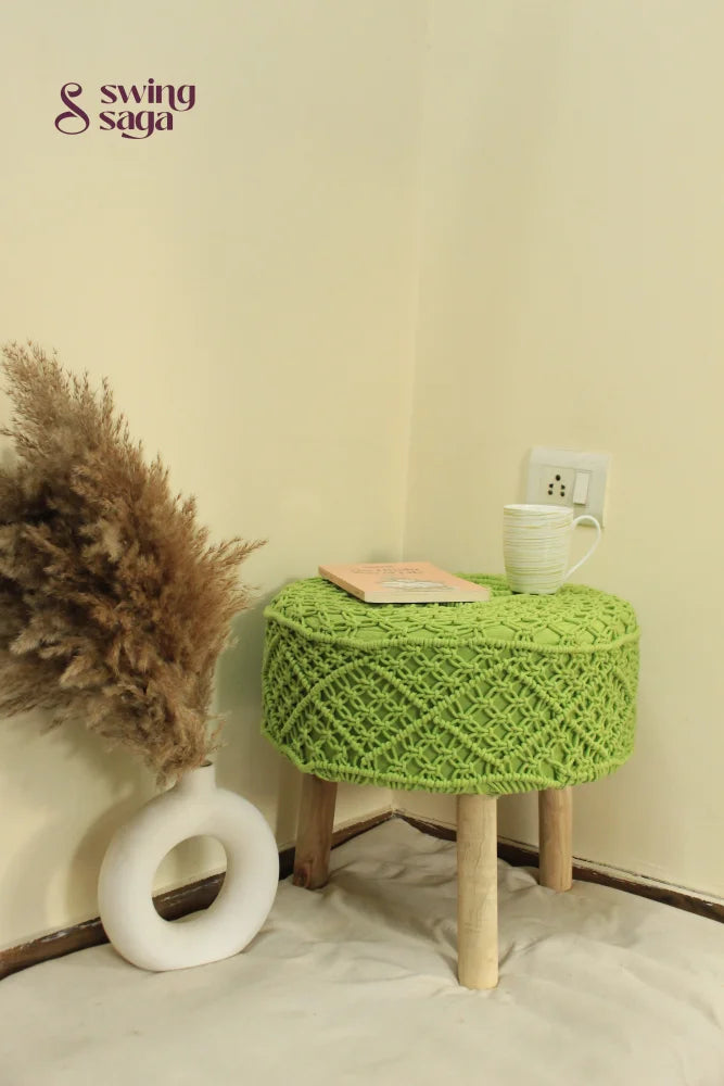 Artisan-crafted green macrame ottoman with wooden legs, ideal for cozy living spaces.